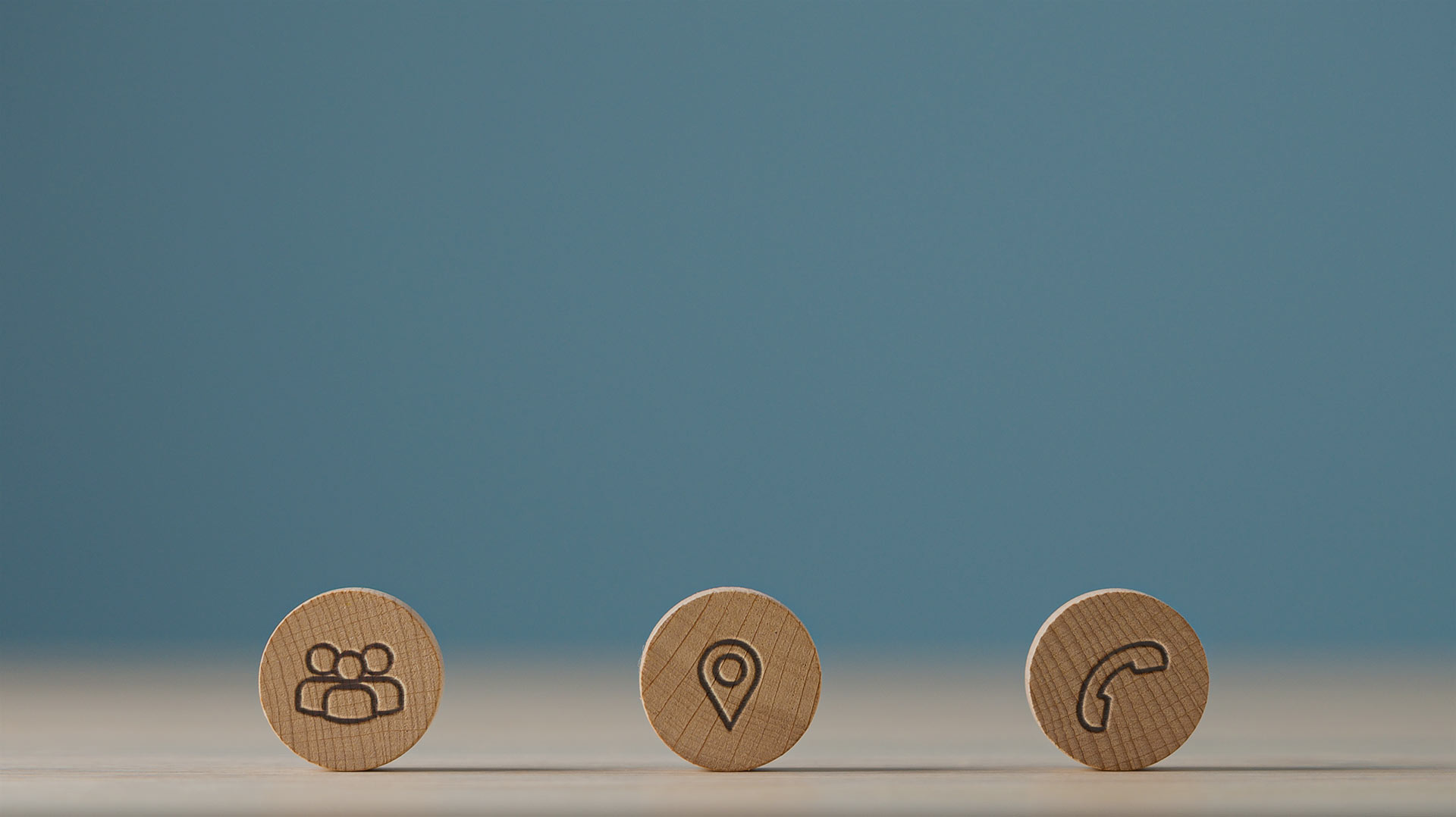 three wooden circles with the first wooden circle with an engraved sketch of three people, the second wooden circle shows a pin for map, and the third wooden circle shows a telephone icon.