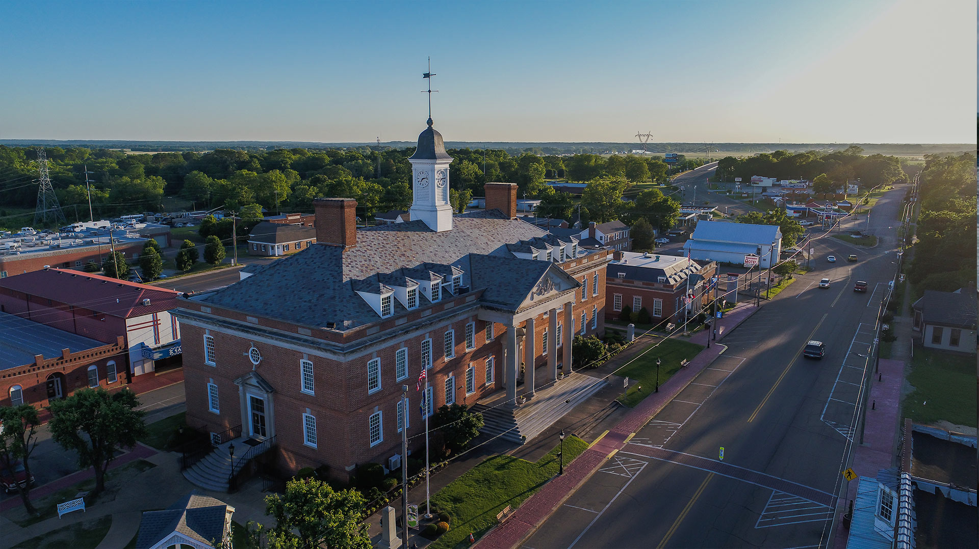 An aerial drone view of the Hardin County Chamber of Commerce building with trees in the background with main road and some cars on the road.